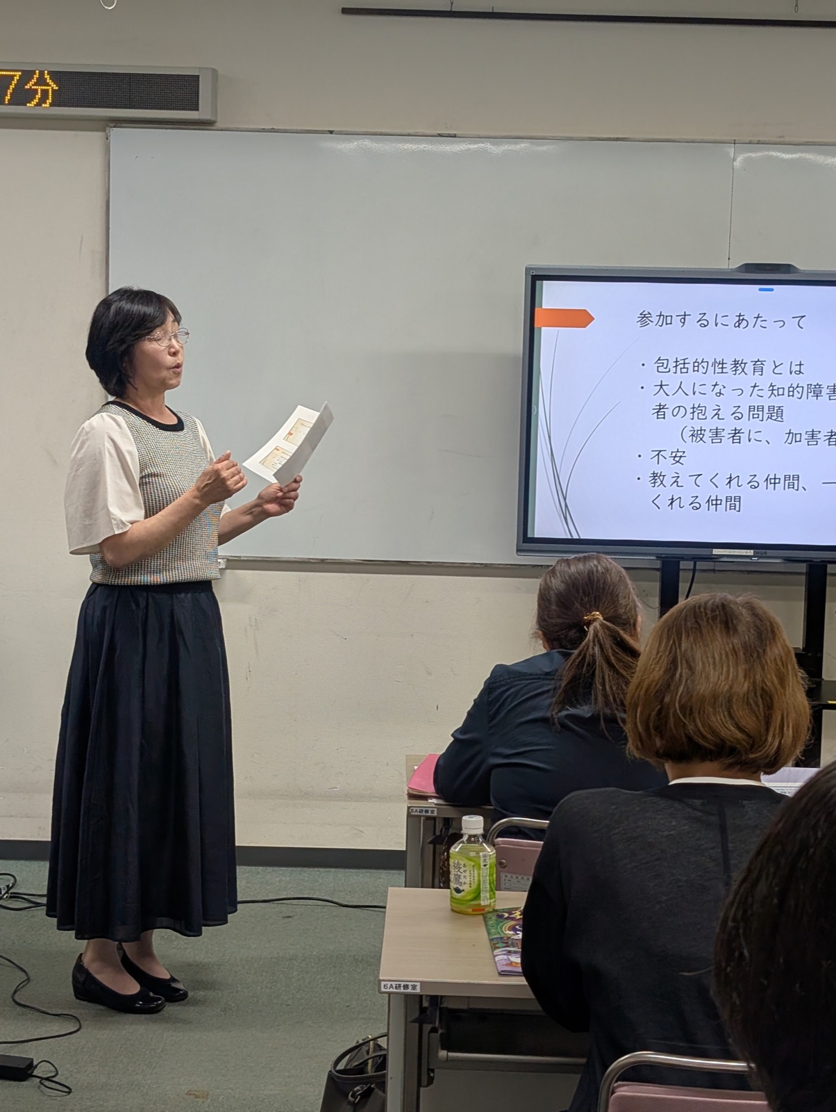 スクリーン横で資料を手に話す講師